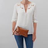 Person wearing a white blouse with bird patterns and blue jeans, holding a brown clutch against a gray background