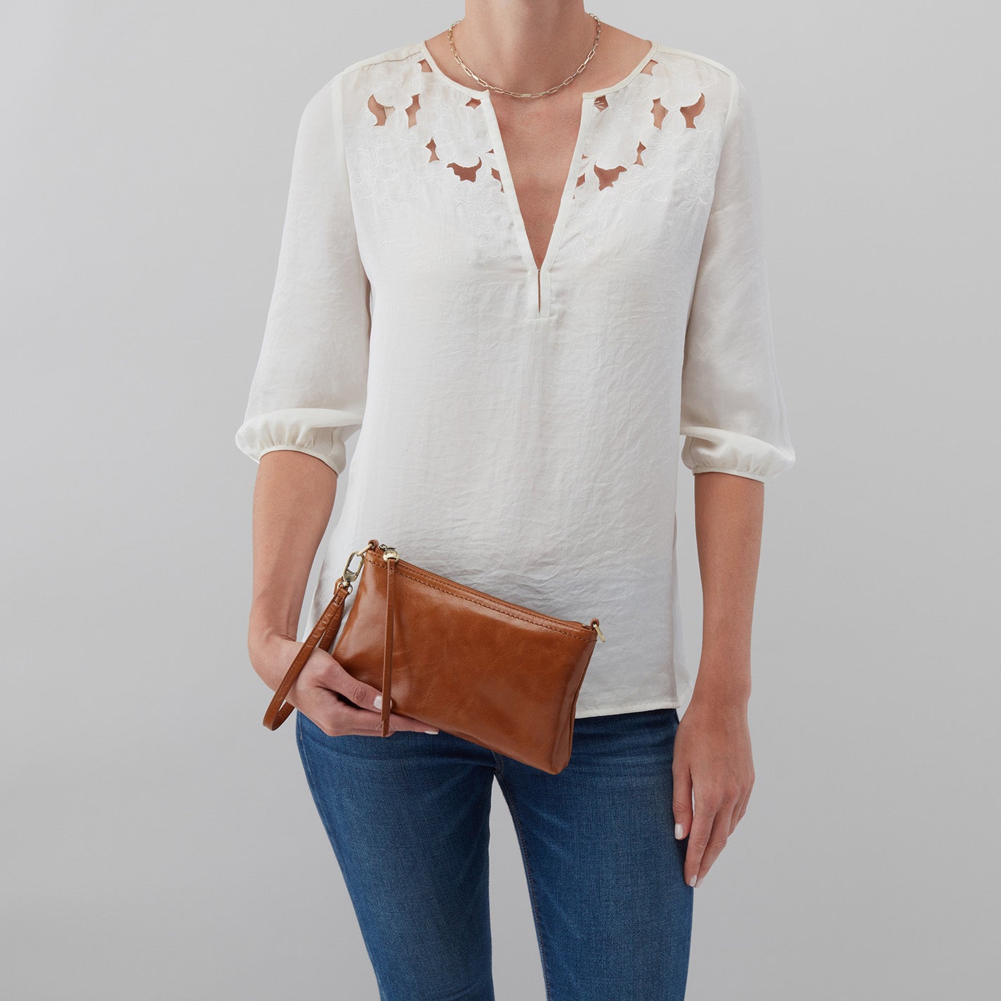 Person wearing a white blouse with bird patterns and blue jeans, holding a brown clutch against a gray background