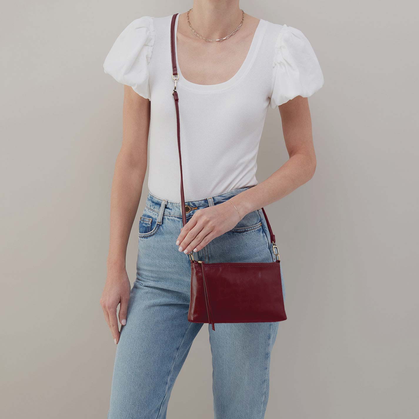 Person wearing a white top and blue jeans with a red handbag on a plain background