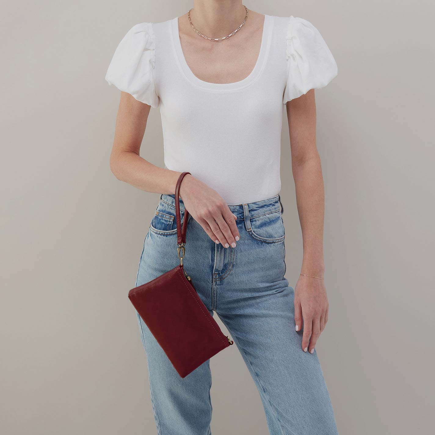 Person wearing a white top and blue jeans holding a red clutch against a neutral background