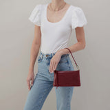 Person wearing a white top and blue jeans, holding a red handbag against a neutral background