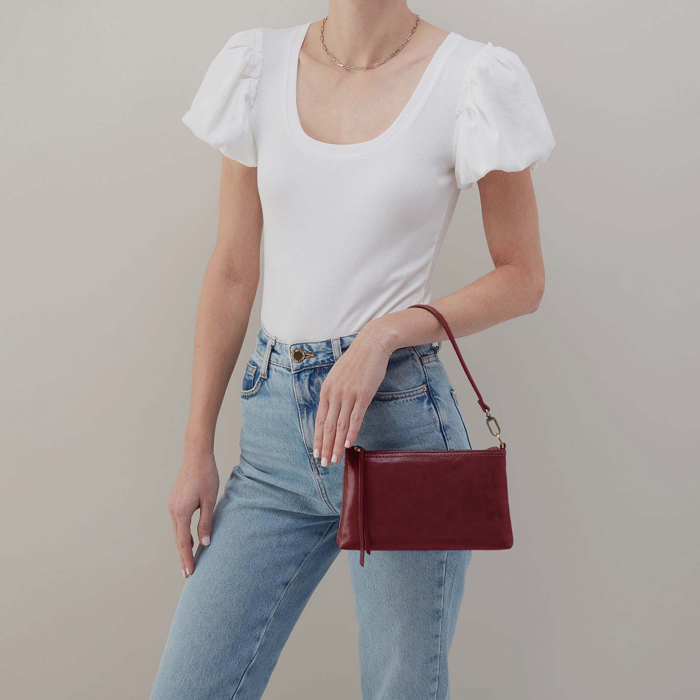Person wearing a white top and blue jeans, holding a red handbag against a neutral background
