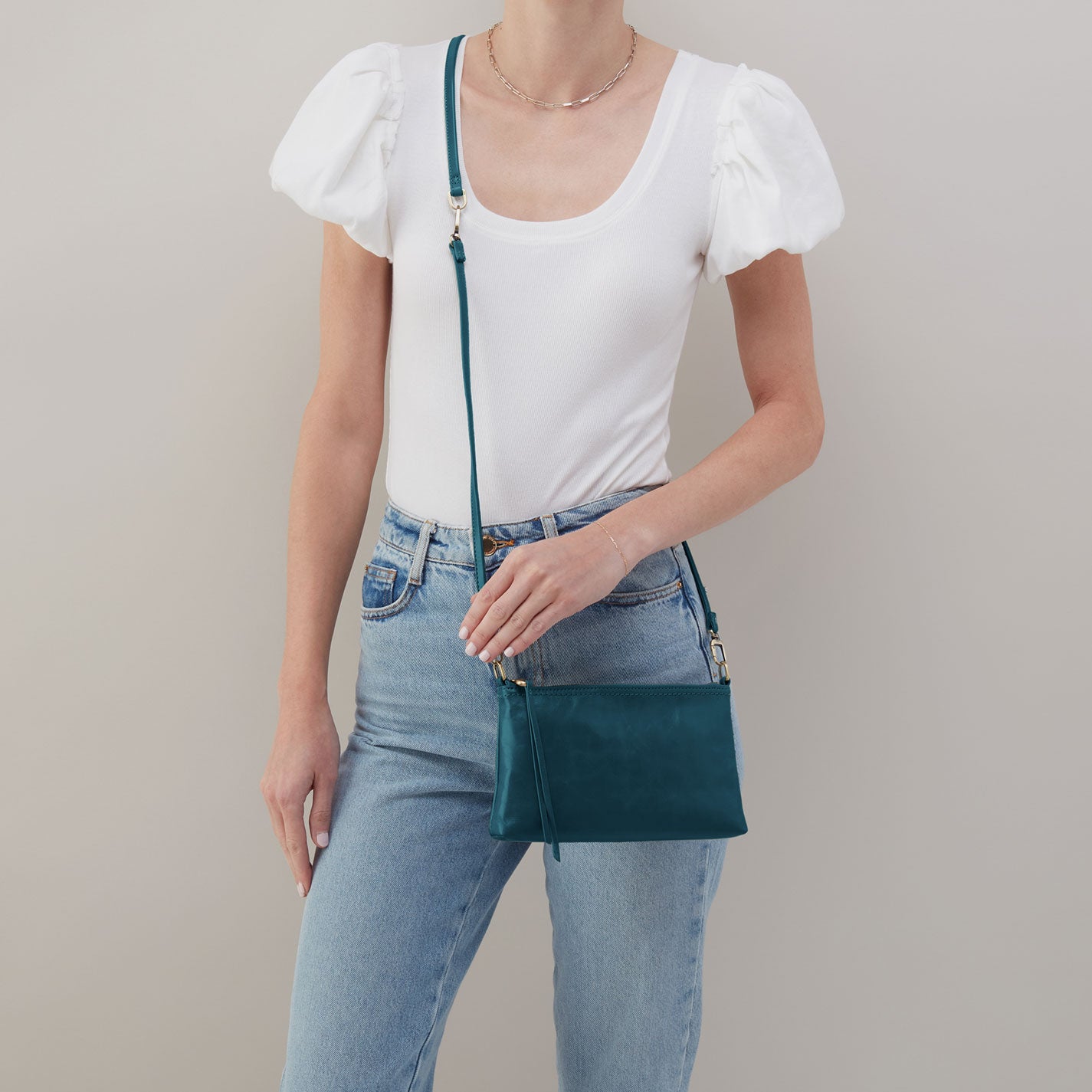 Person wearing a white top and blue jeans with a teal handbag on a plain background