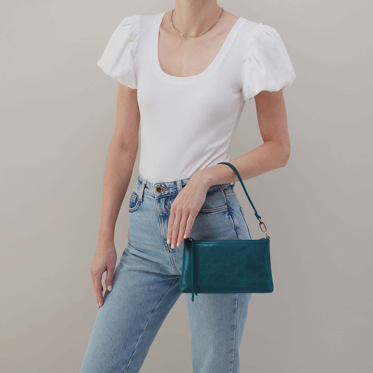 Person wearing a white top and blue jeans holding a green handbag against a plain background