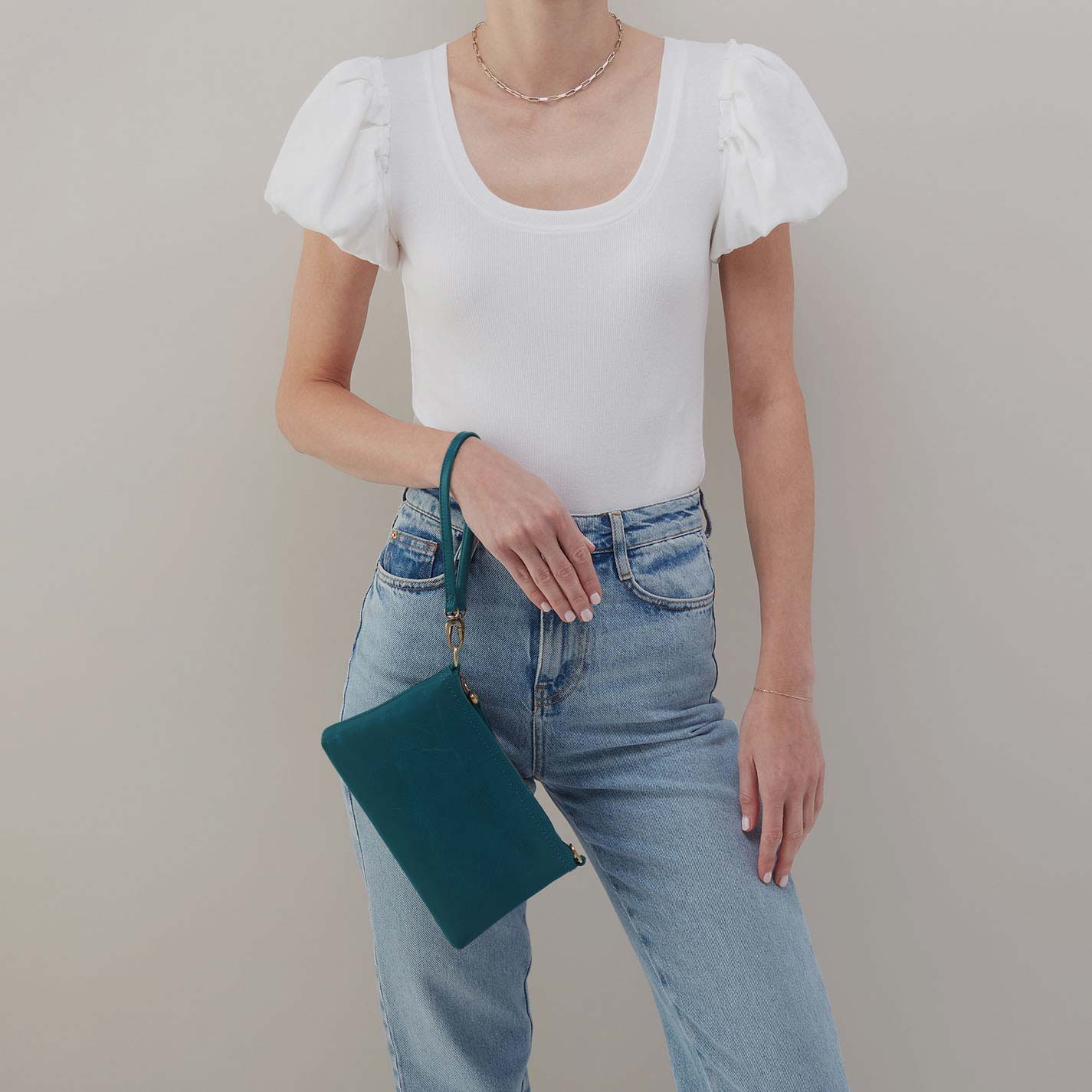 Person wearing a white top and blue jeans holding a green clutch against a plain background