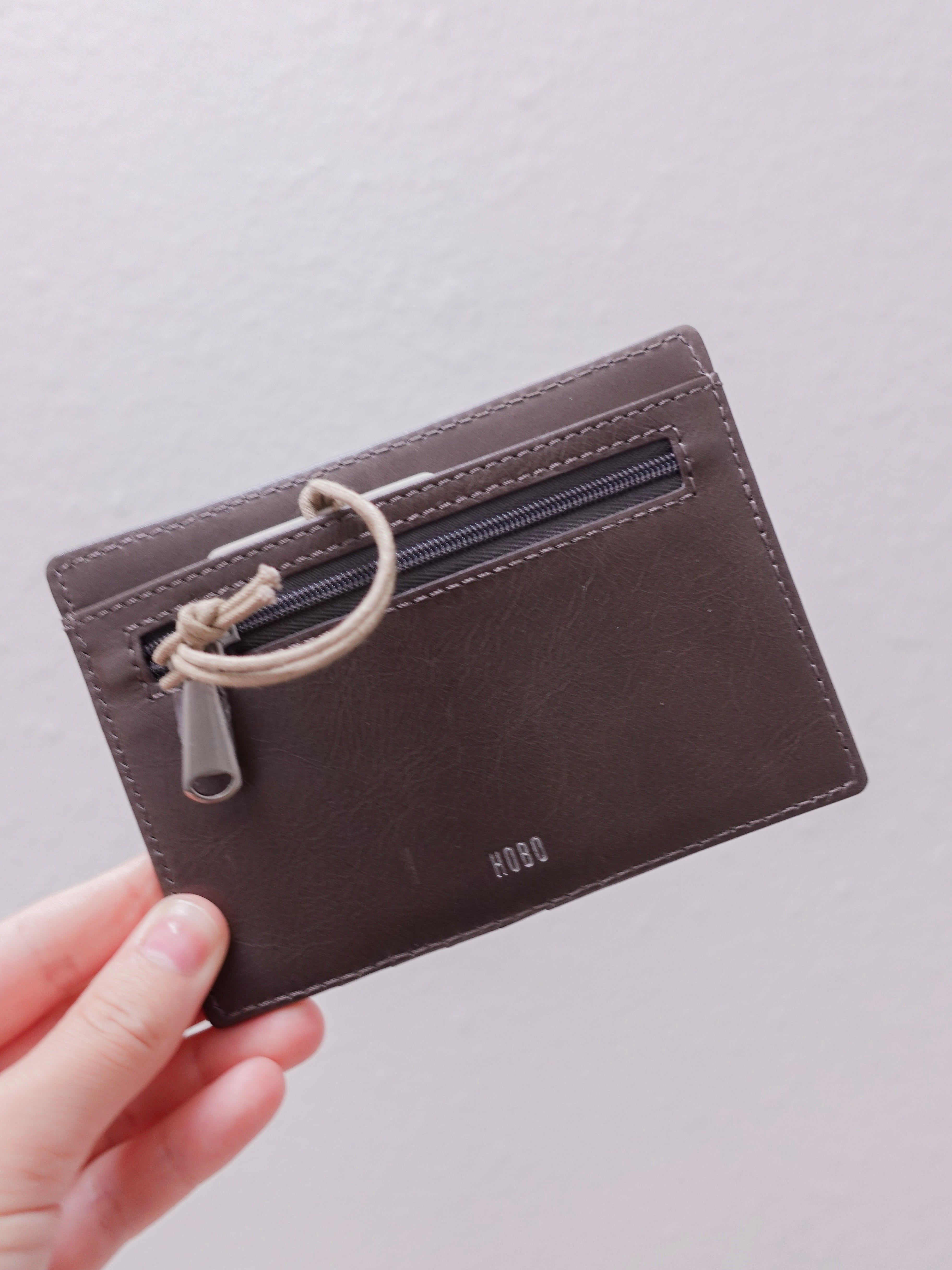 Brown leather wallet with a rope detail held by a hand on a light gray background