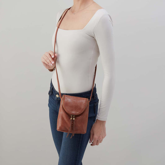 Person holding a brown leather crossbody bag against a plain background