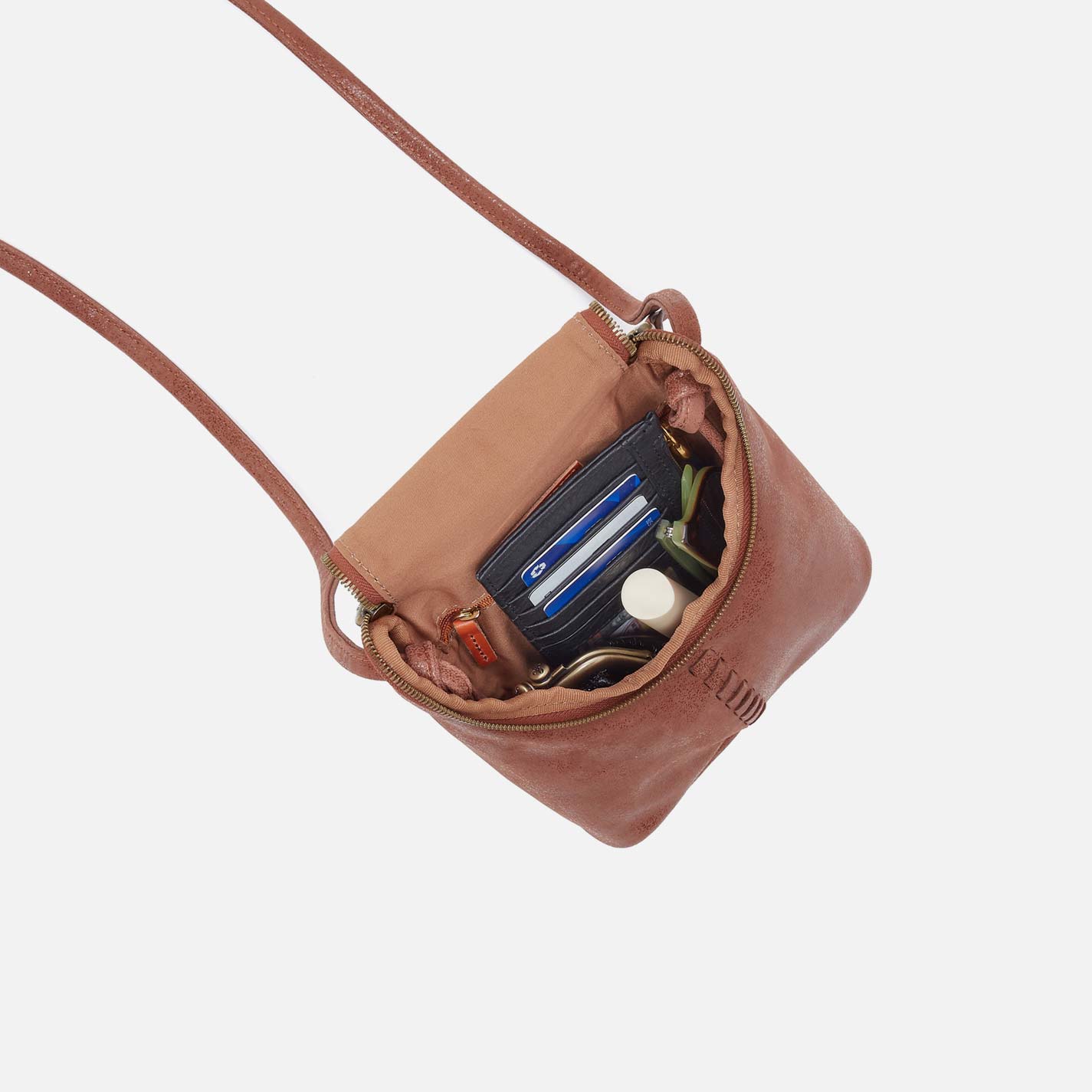 Brown leather crossbody bag with items inside on a light gray background