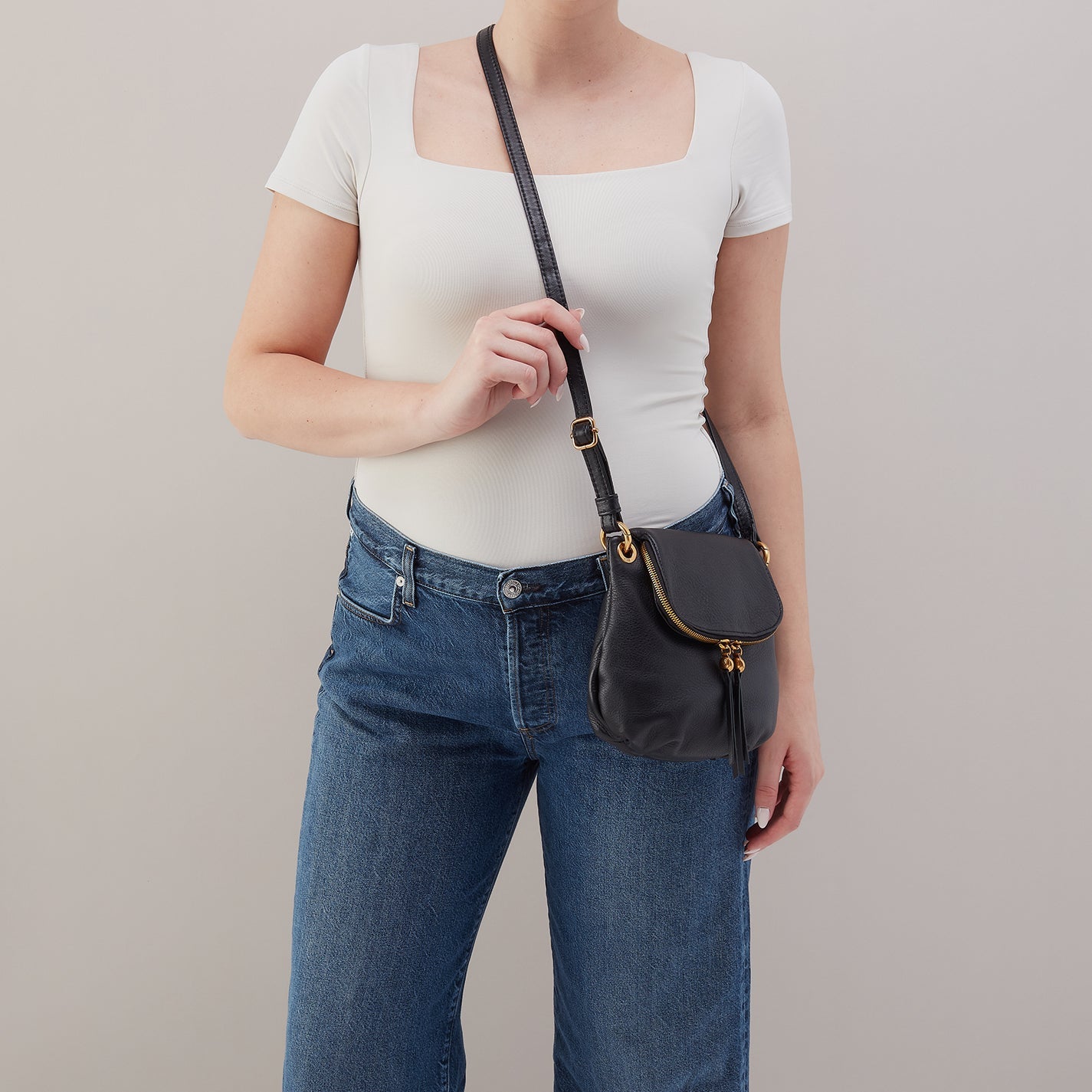 Person wearing a white top and blue jeans holding a black handbag against a plain background