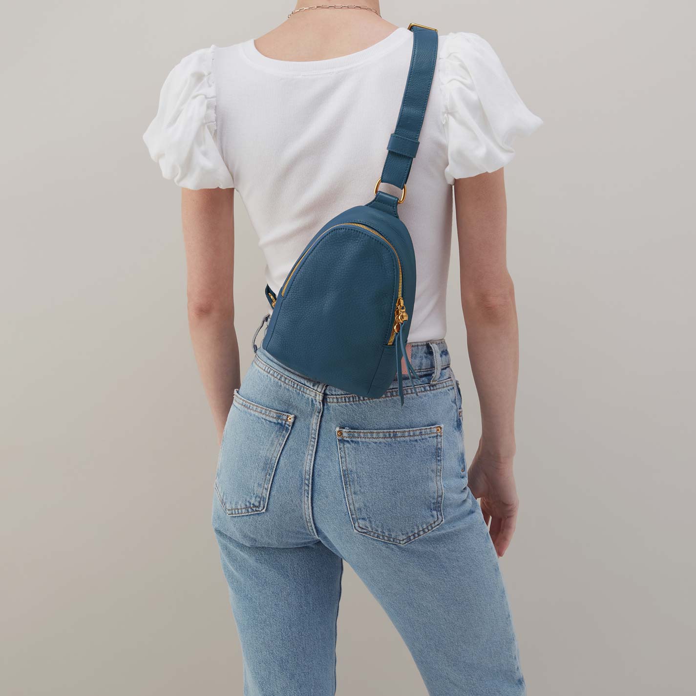 Person wearing a white top and blue jeans with a teal crossbody bag on a plain background