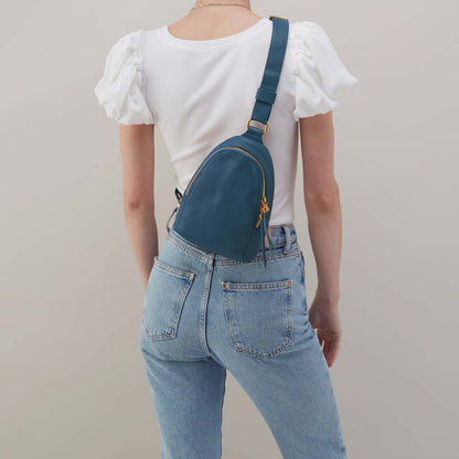 Person wearing a white top and blue jeans with a teal crossbody bag on a plain background
