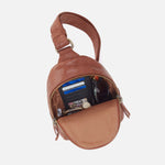 Brown leather sling bag with items inside on a white background