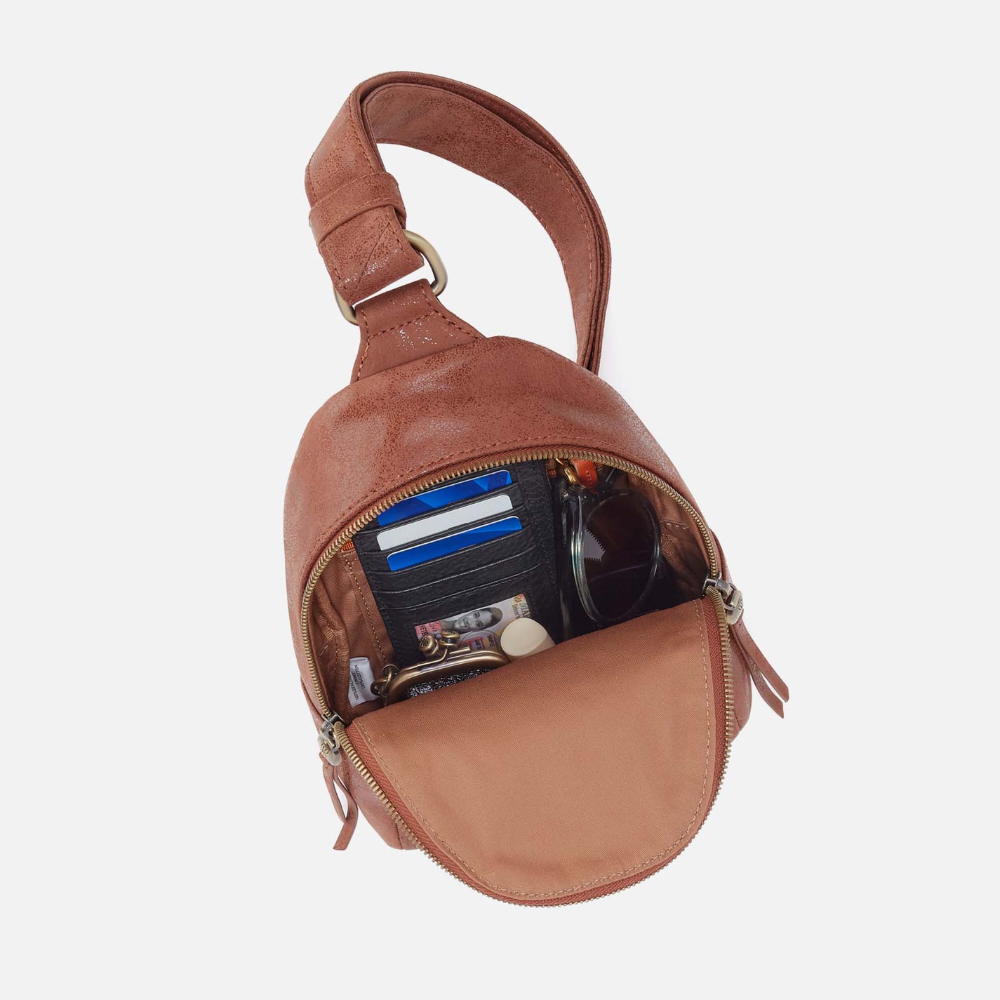 Brown leather sling bag with items inside on a white background