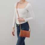 Person holding a brown leather crossbody bag against a plain background