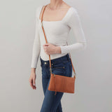 Person holding a brown leather crossbody bag against a plain background