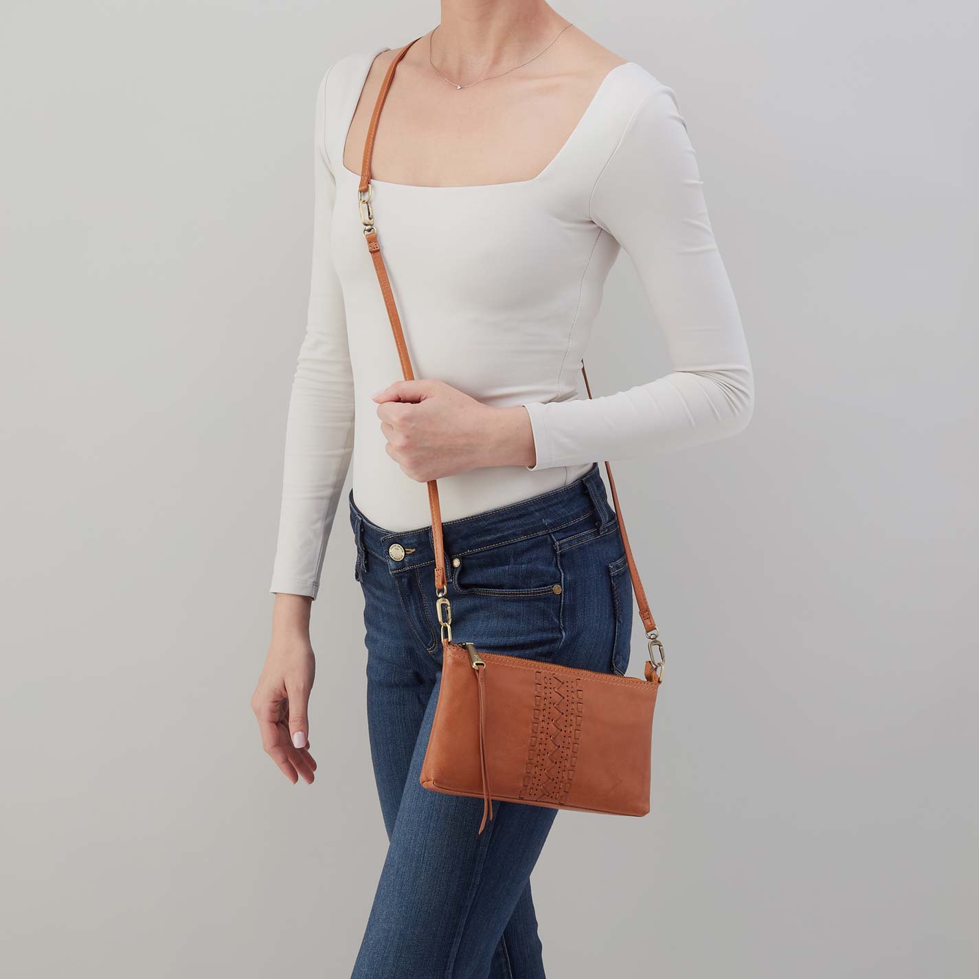 Person holding a brown leather crossbody bag against a plain background