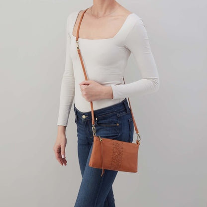 Person holding a brown leather crossbody bag against a plain background