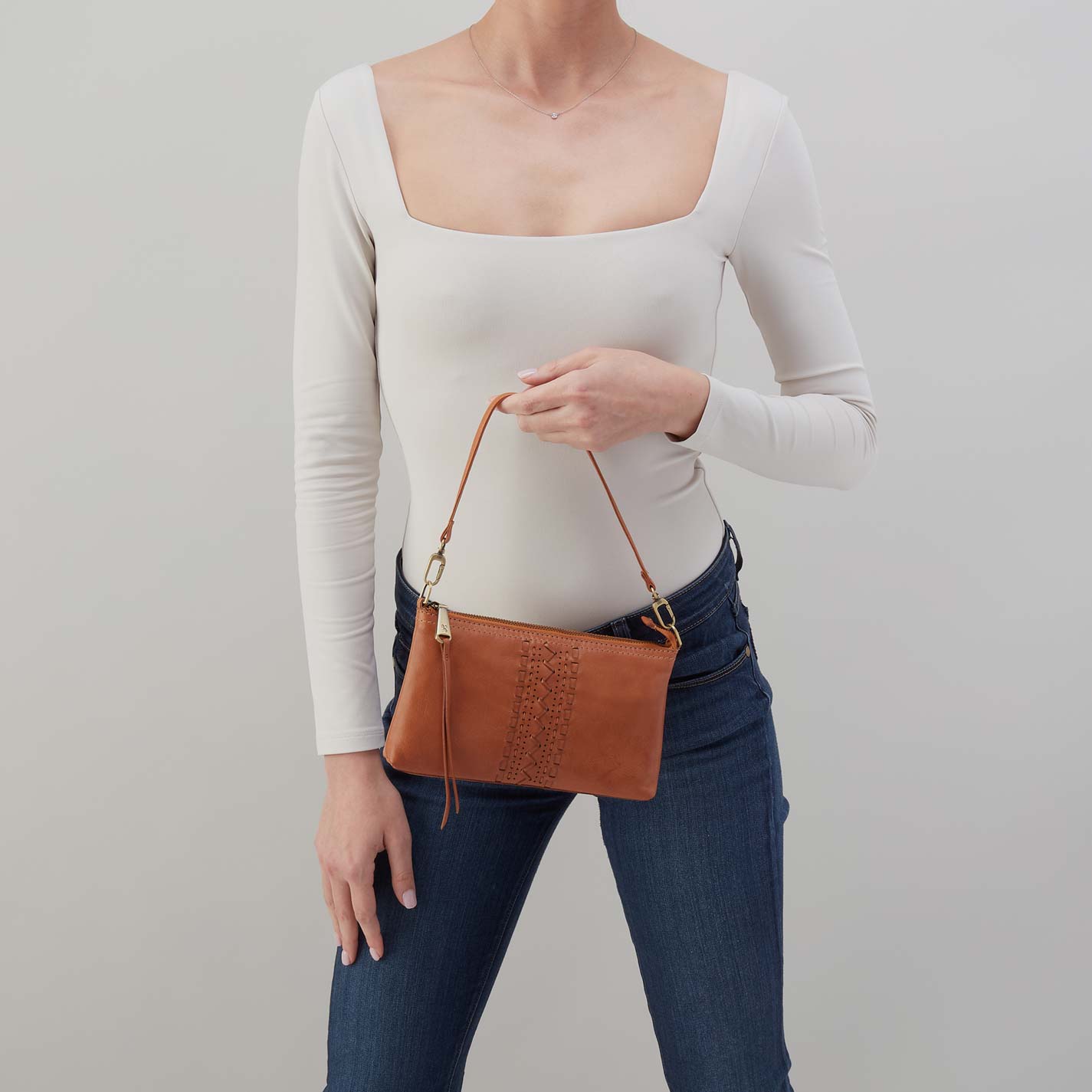 Person holding a brown leather handbag against a plain background
