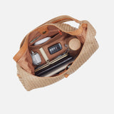 Open straw bag with various items on a light gray background