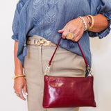 Person wearing a blue embroidered blouse, beige pants, and gold jewelry, holding a red handbag.