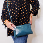 Person wearing a black polka dot shirt holding a blue handbag against a white background