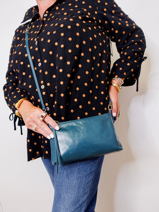 Person wearing a black polka dot shirt holding a blue handbag against a white background