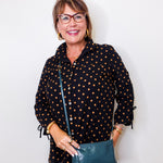 Woman wearing a black polka dot shirt holding a green purse against a white background