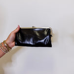Hand holding a black clutch against a plain background