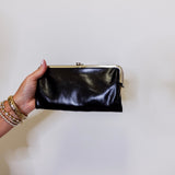 Hand holding a black clutch against a plain background