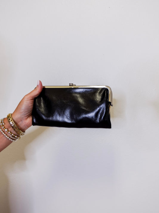Hand holding a black clutch against a plain background