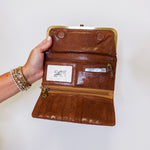 Brown leather clutch with gold clasp held by a hand on a white background