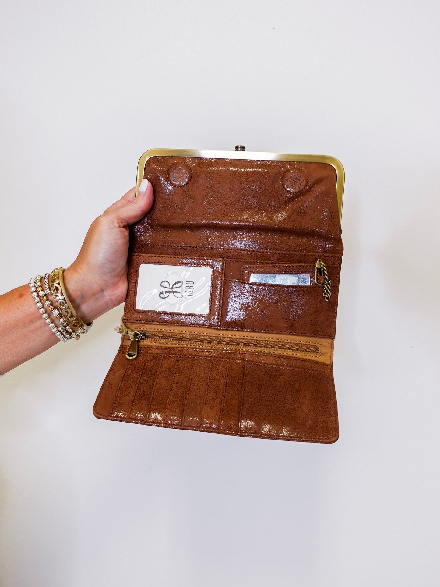 Brown leather clutch with gold clasp held by a hand on a white background