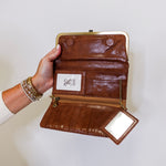Brown leather wallet with gold accents held by a hand on a white background