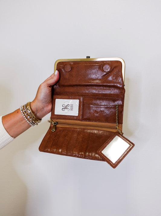 Brown leather wallet with gold accents held by a hand on a white background