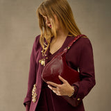 Woman holding a maroon handbag against a neutral background