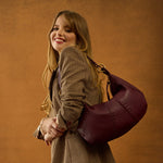 Woman holding a maroon handbag against an orange background
