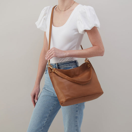 Person wearing a white top and blue jeans holding a brown leather handbag against a neutral background