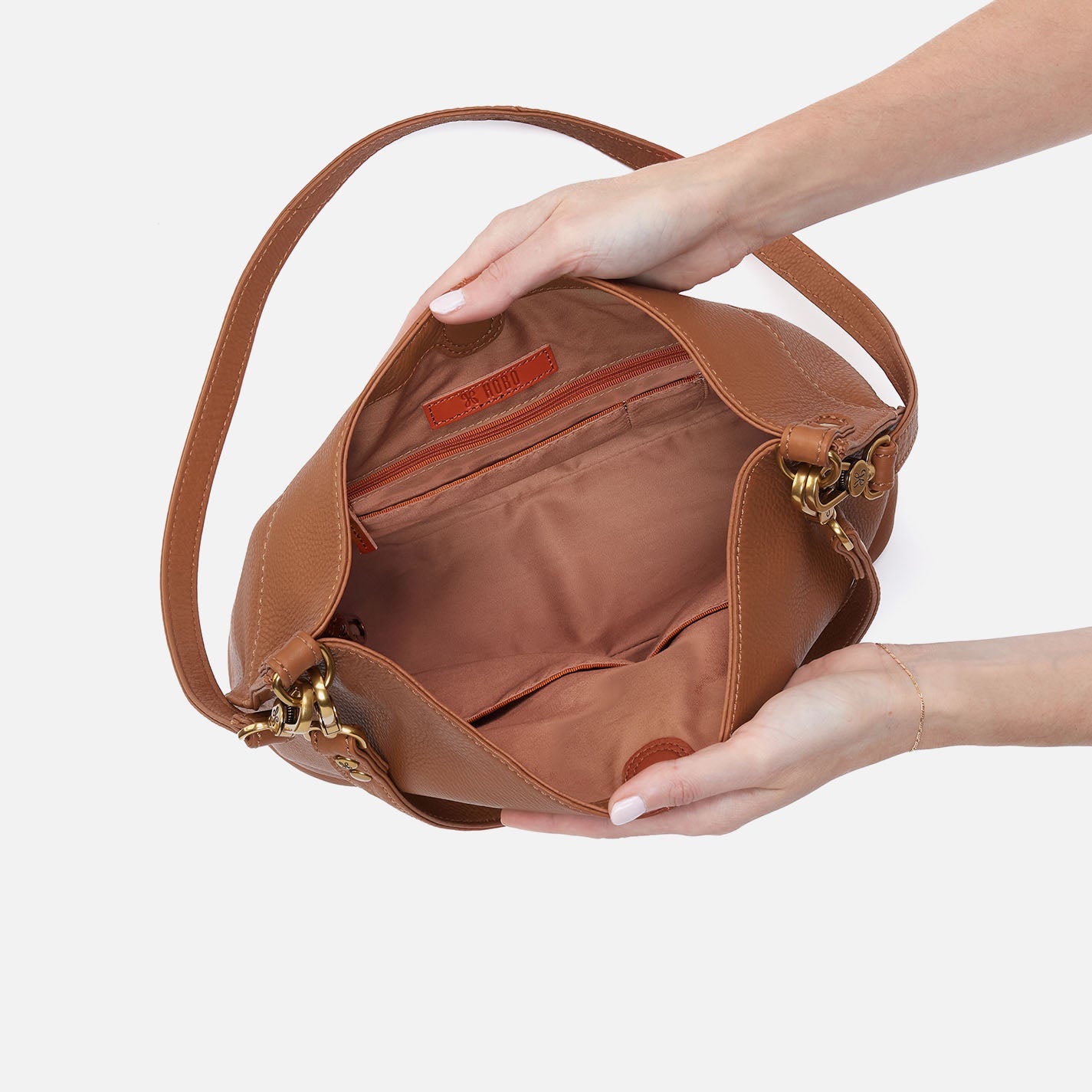 Brown leather handbag held by a person against a light background