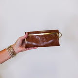 Brown leather clutch held by a hand against a white background