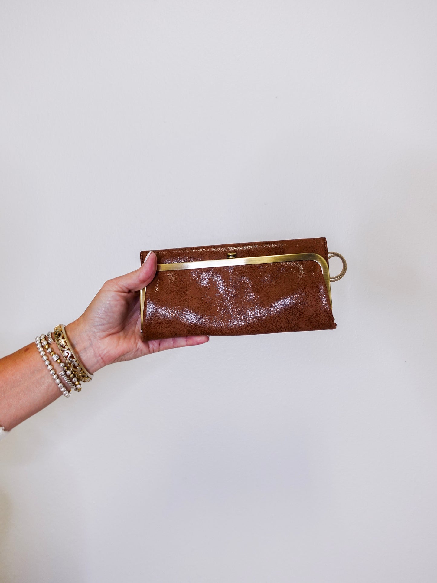Brown leather clutch held by a hand against a white background