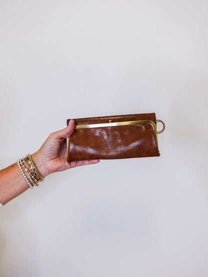 Brown leather clutch held by a hand against a white background