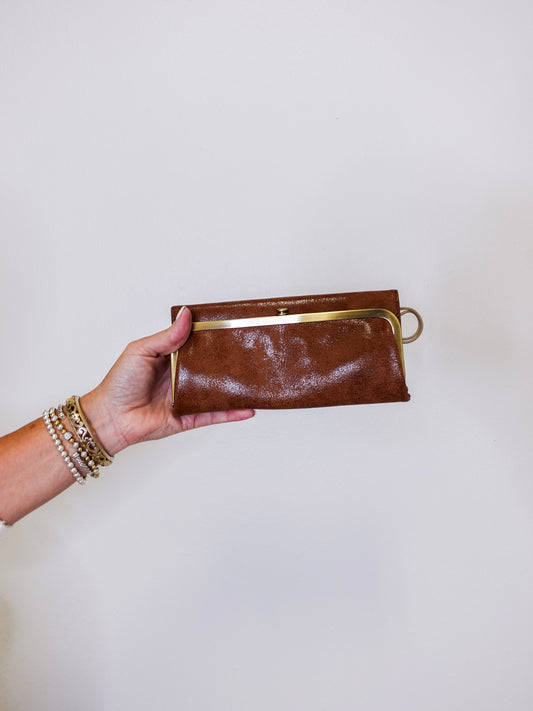 Brown leather clutch held by a hand against a white background