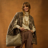 Woman in a plaid coat and brown pants holding a beige handbag against a brown background