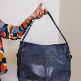 Person holding a blue leather handbag against a plain background