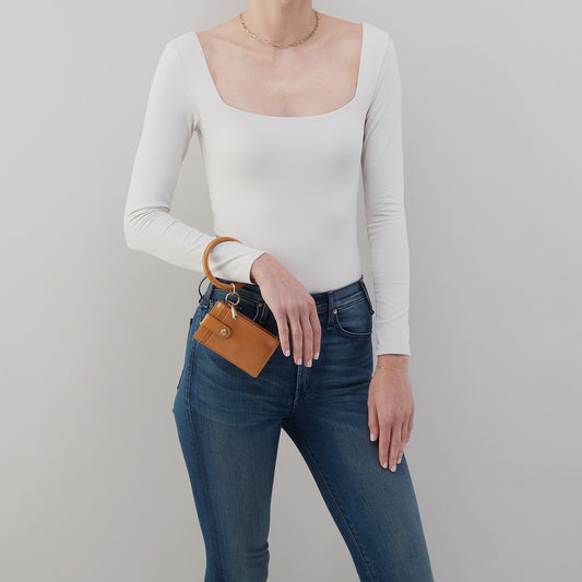 Person wearing a white long-sleeve top and blue jeans, holding a brown leather wallet.