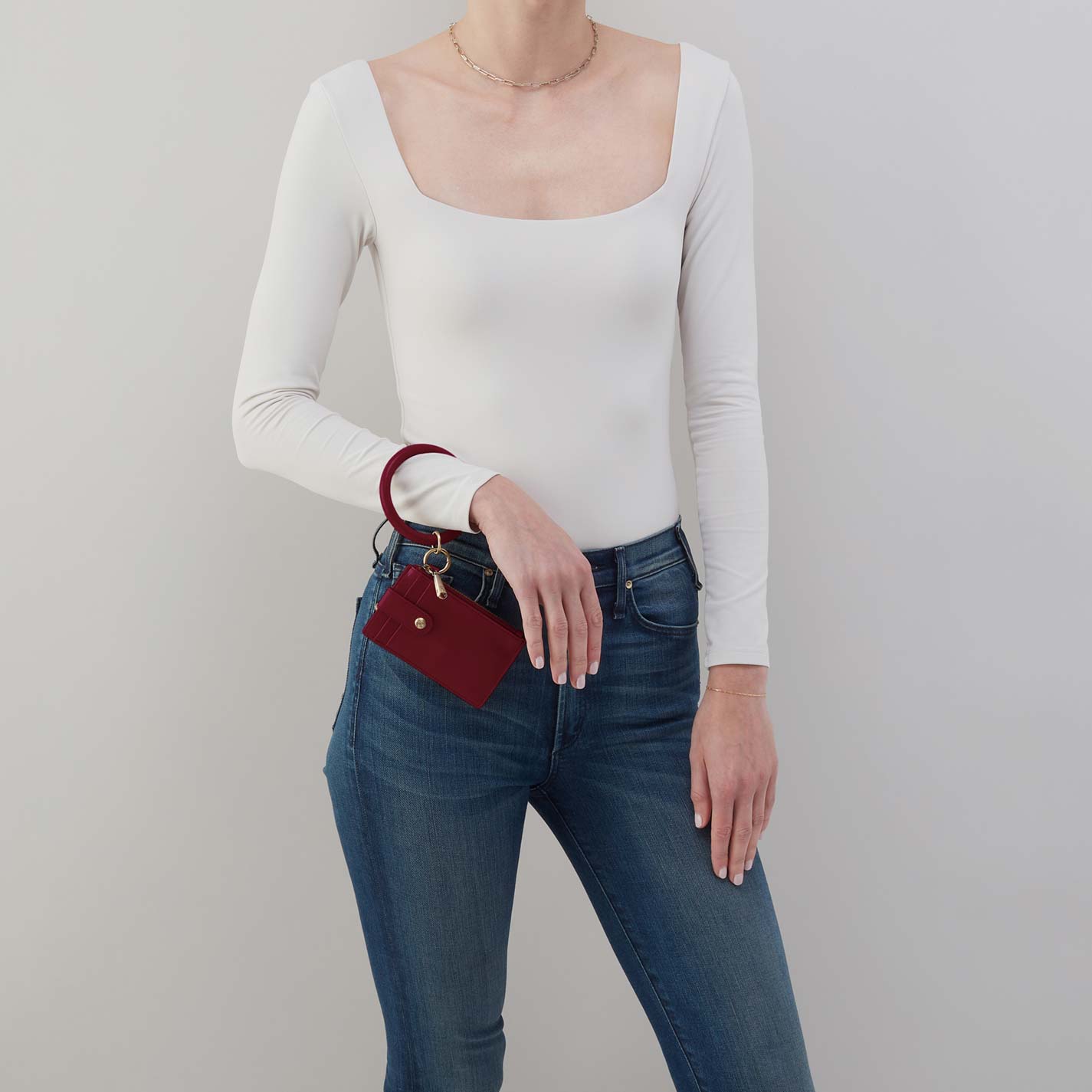 Person wearing a white long-sleeve top and blue jeans, holding a red wallet.