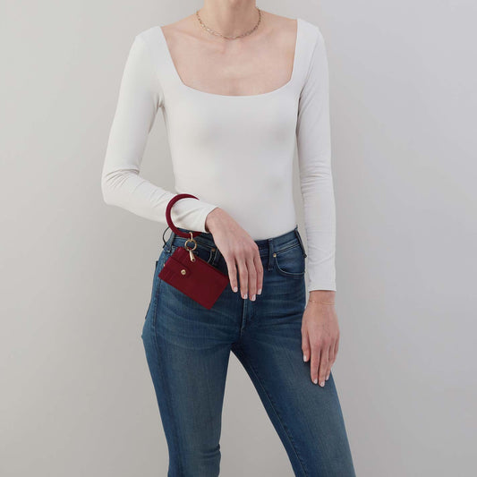 Person wearing a white long-sleeve top and blue jeans, holding a red wallet.