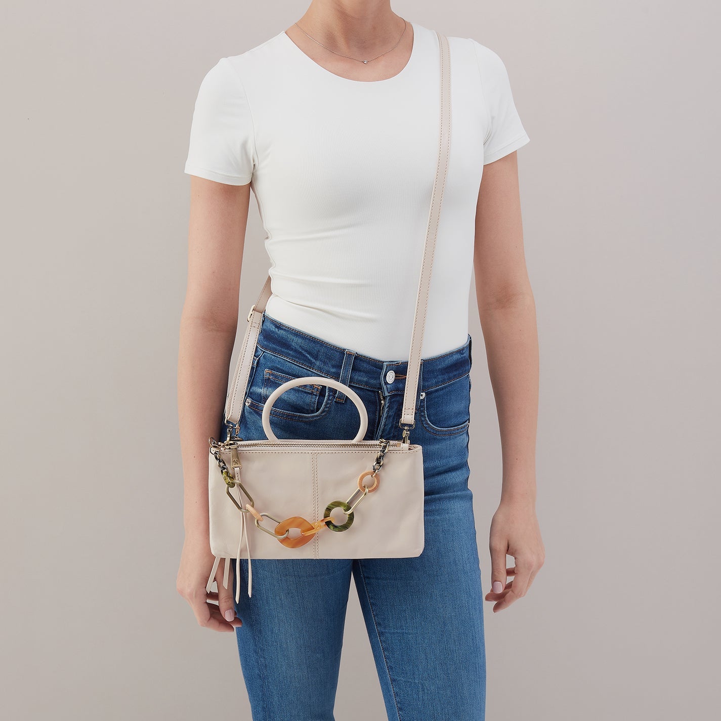 Person wearing a white t-shirt and blue jeans with a beige handbag on a plain background