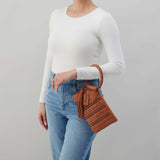 Person wearing a white long-sleeve top and blue jeans, holding a brown leather handbag against a gray background