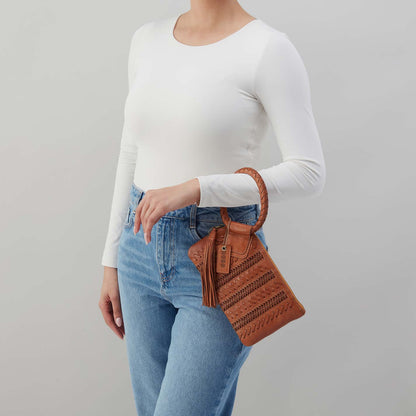 Person wearing a white long-sleeve top and blue jeans, holding a brown leather handbag against a gray background